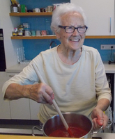 Ältere Frau rührt fröhlich in einem Topf mit roter Sauce.