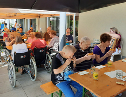 Ältere Menschen sitzen draußen zusammen und genießen Essen und Getränke.