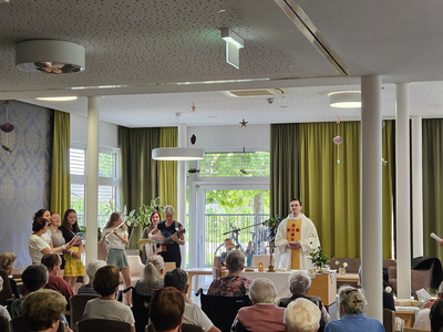 Eine Gruppe singt im Raum, während ein Priester ihnen zuhört.