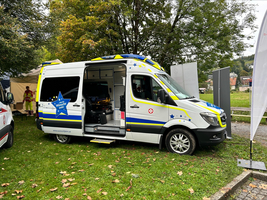Ein Krankenwagen mit geöffneten Türen steht auf einer Wiese.