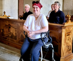 Eine Person im Rollstuhl sitzt in einer Kirche und lächelt.