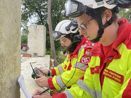 Zwei Feuerwehrleute in Schutzkleidung arbeiten konzentriert mit Geräten und Notizen.