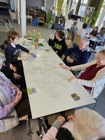 Gruppen von Menschen spielen an einem Tisch mit Karten in einem Gemeinschaftsraum.