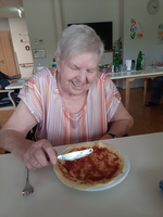 Eine lächelnde ältere Frau isst einen Pfannkuchen mit Marmelade.