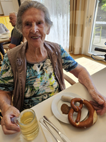 Eine ältere Frau lächelt und hält eine Brezel sowie ein Glas Bier.