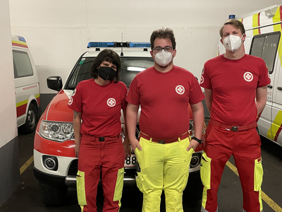 Drei Rettungssanitäter in Uniform stehen vor einem Einsatzfahrzeug.