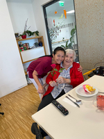 Eine lächelnde Frau umarmt eine ältere Dame mit einer Rose in der Hand.