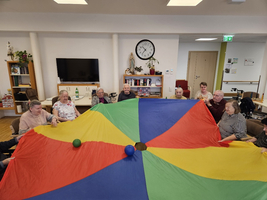 Ältere Menschen spielen gemeinsam mit einem großen, bunten Fallschirm.
