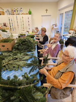 Senioren basteln gemeinsam mit Tannenzweigen in einem gemütlichen Raum.