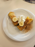 Ein Teller mit gefüllten Crêpes, Sahne und Bananenscheiben.