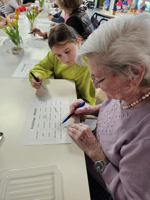 Eine ältere Frau und ein Kind spielen Frühlings-Bingo an einem Tisch.