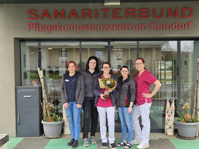 Fünf Mitarbeiterinnen des Samariterbundes, die vor dem Pflegekompetenzzentrum Kaindorf stehen. Eine Frau hält einen Blumenstrauß. Das Gebäude ist modern und einladend gestaltet.