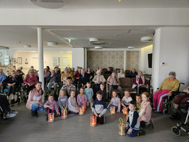 Kinder mit Laternen stehen vor Senioren in einem Gemeinschaftsraum.