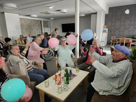 Ältere Menschen feiern und jonglieren mit Ballons in einem Gemeinschaftsraum.
