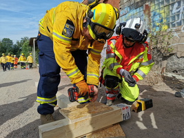 Zwei Einsatzkräfte arbeiten zusammen an einer Holzplatte mit einem Akku-Bohrer.