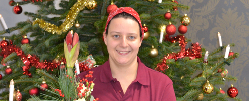 Frau mit einem Blumenstrauß steht vor einem festlich geschmückten Weihnachtsbaum.