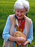 Eine ältere Frau hält ein Kaninchen in ihren Armen und lächelt freundlich.