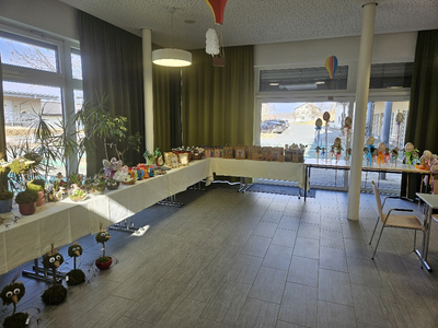 Raum mit gedeckten Tischen voller kunstvoll dekorierter Ostereier und Bastelarbeiten.