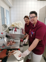 Zwei Frauen schneiden Fleisch mit einer Aufschnittmaschine in einer Metzgerei.