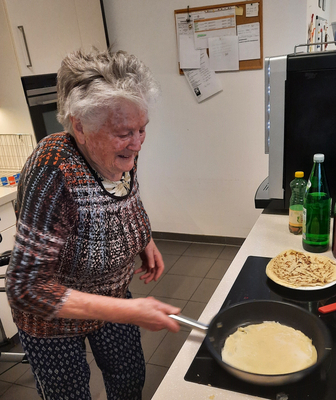 Eine ältere Frau brät einen Pfannkuchen in der Küche.