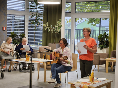Eine Frau singt und spielt Gitarre, während andere zuhören.