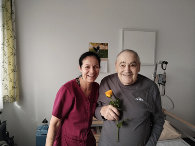 Eine Frau und ein älterer Mann lächeln, während er eine Rose hält.