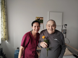 Eine Frau und ein älterer Mann lächeln, während er eine Rose hält.