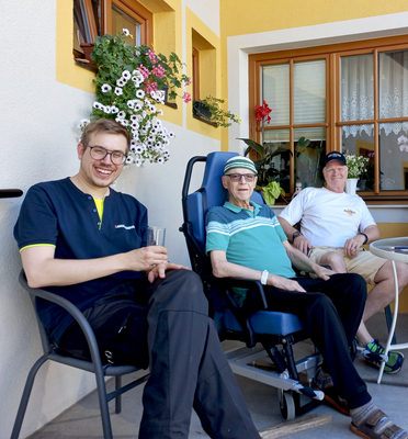 Drei Männer sitzen entspannt auf einer Terrasse und genießen die Sonne.