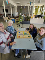 Ältere Frauen und Mädchen spielen ein Brettspiel in einem gemütlichen Gemeinschaftsraum.