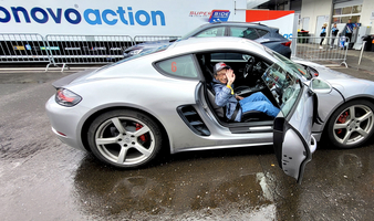 Ein Mann sitzt in einem silbernen Sportwagen und winkt freundlich.