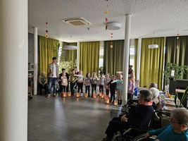 Kinder stehen mit Laternen auf einer Bühne, während Senioren zuschauen.