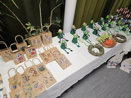 Bunte Handarbeiten und Froschfiguren auf einem Tisch, dekoriert mit Blumenmotiven.