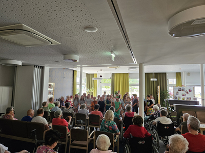 Gruppenvorführung von Kindern vor älteren Menschen in einem Gemeinschaftsraum.