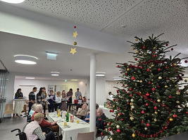 Weihnachtsfeier mit einem großen Weihnachtsbaum und Bewohnern in einem Gemeinschaftsraum.