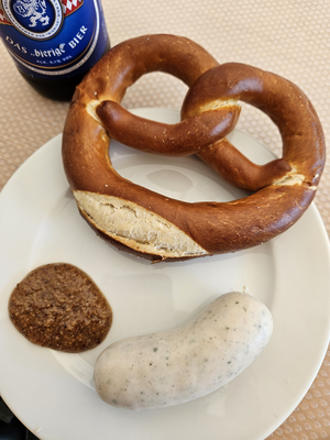 Brezel mit Weißwurst und süßem Senf auf einem Teller.