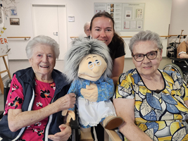 Drei Frauen lächeln zusammen, eine hält eine Handpuppe.