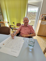 Älterer Mann sitzt am Tisch und löst ein Wortsuche-Rätsel.