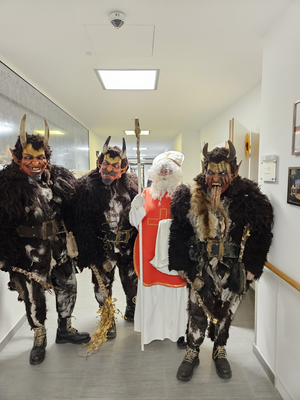 Vier verkleidete Figuren in einer Flur, zwei teufelsähnlich und eine als Nikolaus.