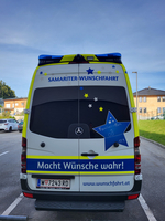 Ein Fahrzeug mit der Aufschrift „Macht Wünsche wahr!“ steht auf einem Parkplatz.