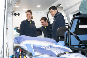 Drei Personen lächeln und stehen im Inneren eines Ambulanzfahrzeugs.