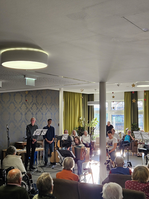 Musikaufführung in einem Saal mit sitzenden Zuschauern und Musikergruppen.