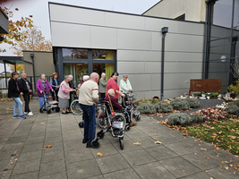 Gruppe älterer Menschen mit Rollatoren vor einem Gebäude im Freien.