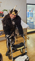 Ein verkleideter Krampus steht mit einem Rollator in einem Raum.