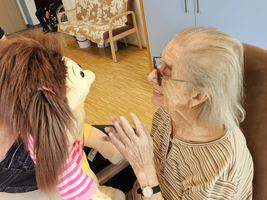 Eine ältere Frau unterhält sich lachend mit einer Stoffpuppe.