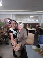 Zwei Frauen tanzen fröhlich mit lustigen Hüten in einem Gemeinschaftsraum.