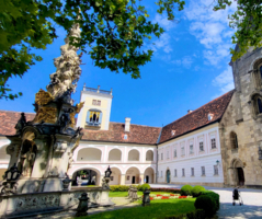 Innenhof eines historischen Gebäudes mit einer Statue und bunten Blumenbeeten.