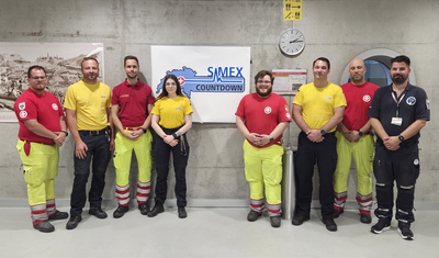 Gruppenbild von Rettungskräften mit unterschiedlichfarbigen Uniformen vor einem Countdown-Schild.