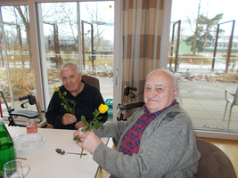 Zwei ältere Männer halten gelbe Rosen und lächeln.