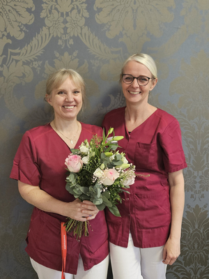 Zwei Frauen in roten Shirts halten einen Blumenstrauß zusammen.