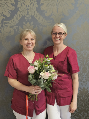 Zwei Frauen in roten Shirts halten einen Blumenstrauß zusammen.